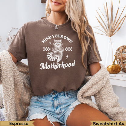 Brown t-shirt with "Mind Your Own Motherhood" text and raccoon graphic.