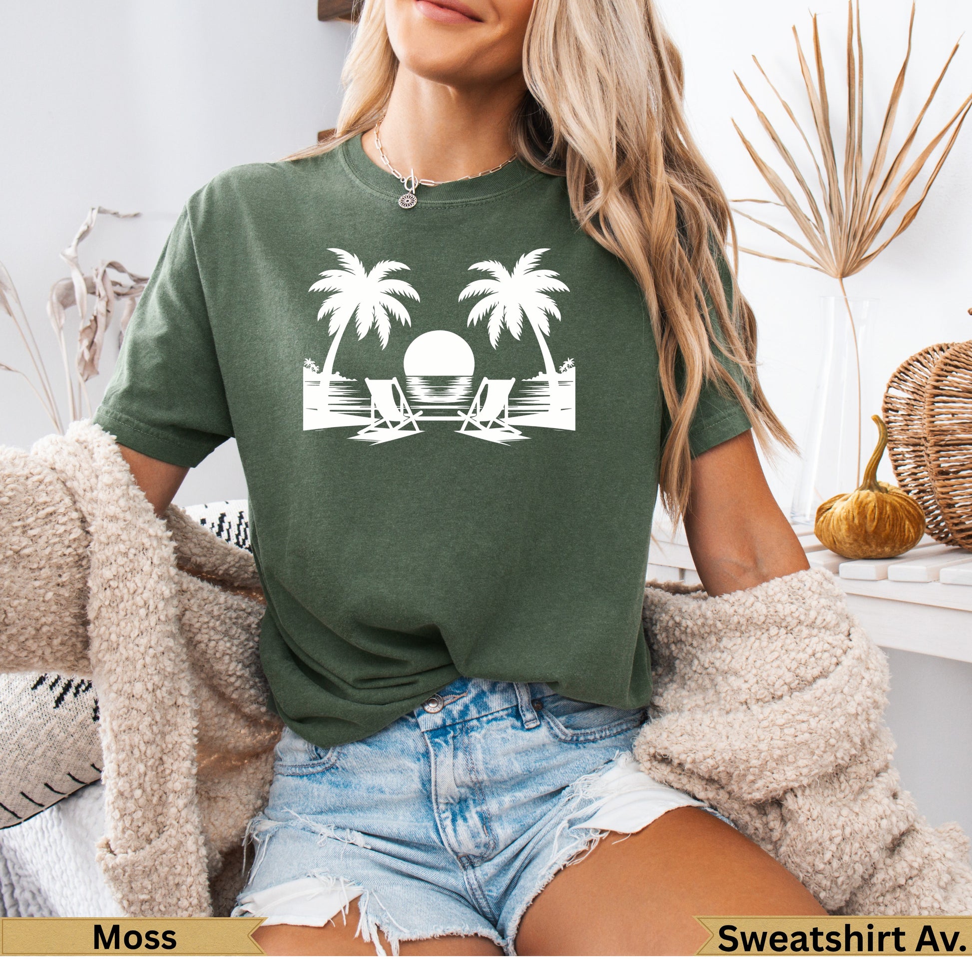 Green t-shirt with white graphic of two palm trees, beach chairs, and sun.