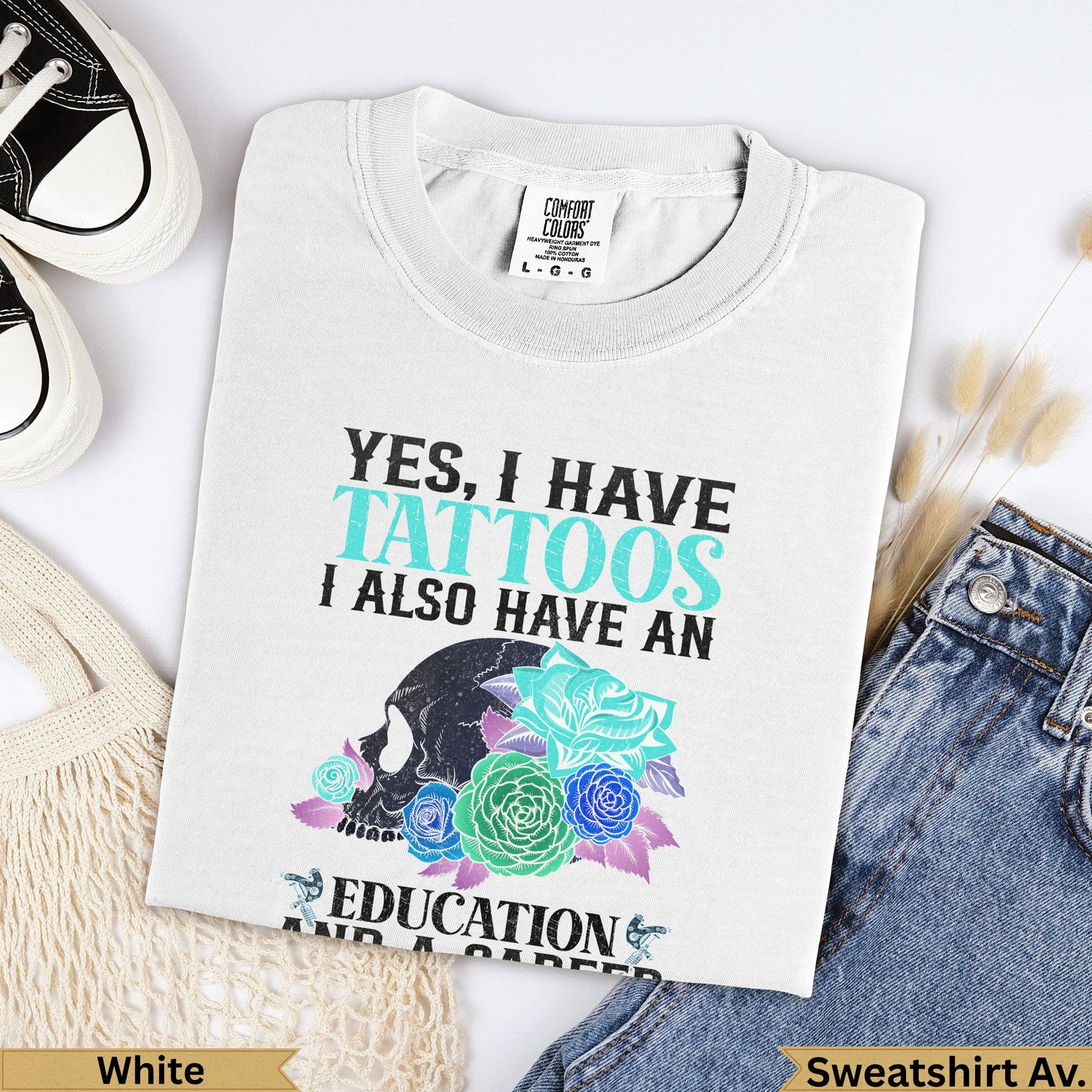 White graphic t-shirt with skull, flowers, and text about tattoos and education.