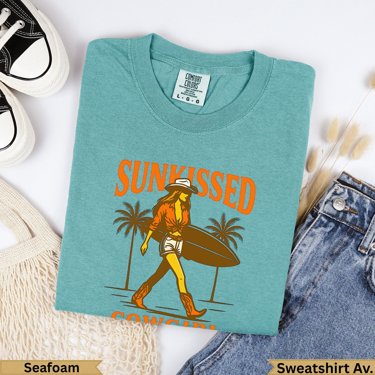 Seafoam Comfort Colors sweatshirt with "Sunkissed" text and cowgirl carrying surfboard.