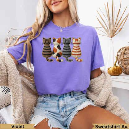Four knitted cats with different patterns on a purple t-shirt.