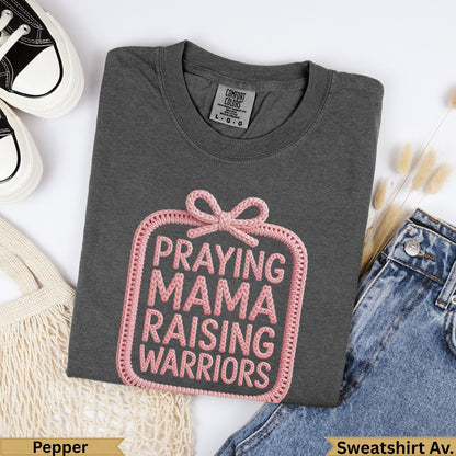 Dark grey sweatshirt with pink "Praying Mama Raising Warriors" graphic.