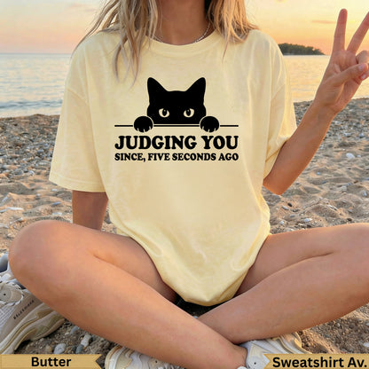 Yellow t-shirt with black cat peeking over, text "JUDGING YOU SINCE, FIVE SECONDS AGO".