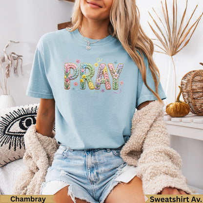 Light blue t-shirt with "PRAY" text in floral and braided letters.