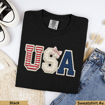 Black t-shirt with "USA" graphic made of patterned patches and a pink bow.