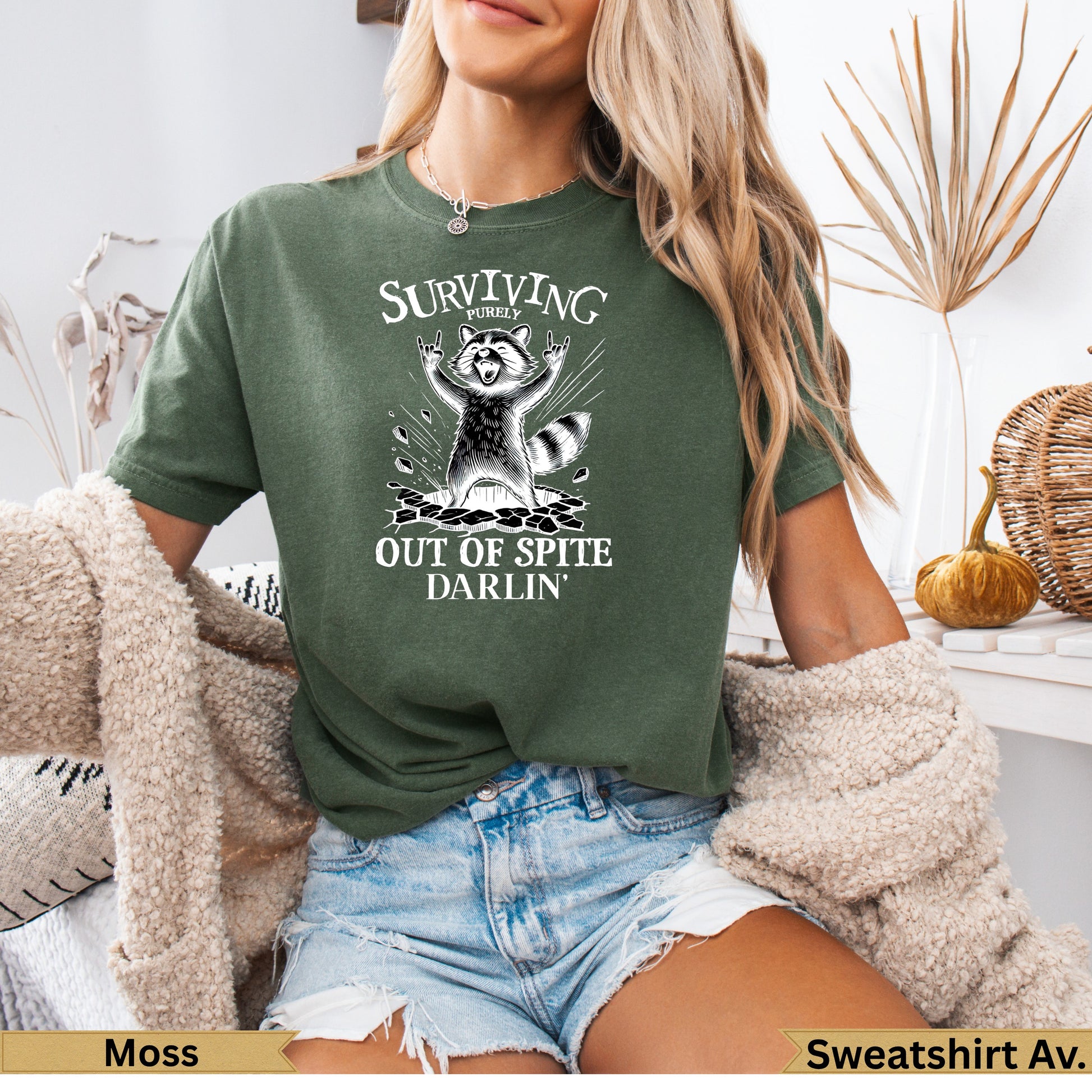 Green t-shirt with raccoon graphic and text "Surviving Purely Out of Spite Darlin'".