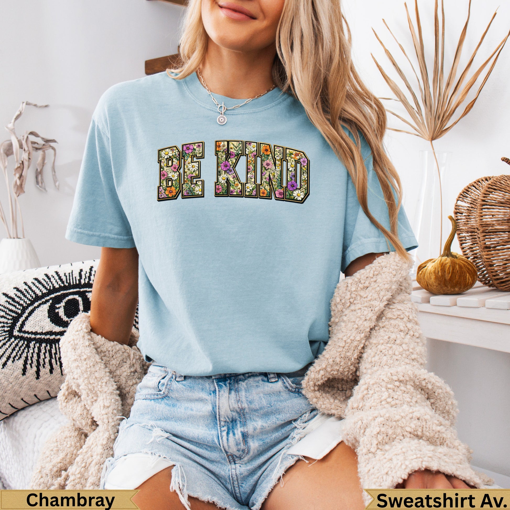 Light blue t-shirt with "BE KIND" in floral text, worn by a model.