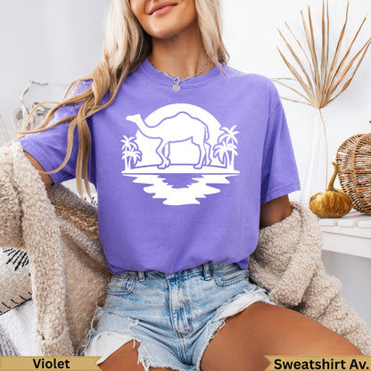White graphic of camel and palm trees in front of sun on purple t-shirt.