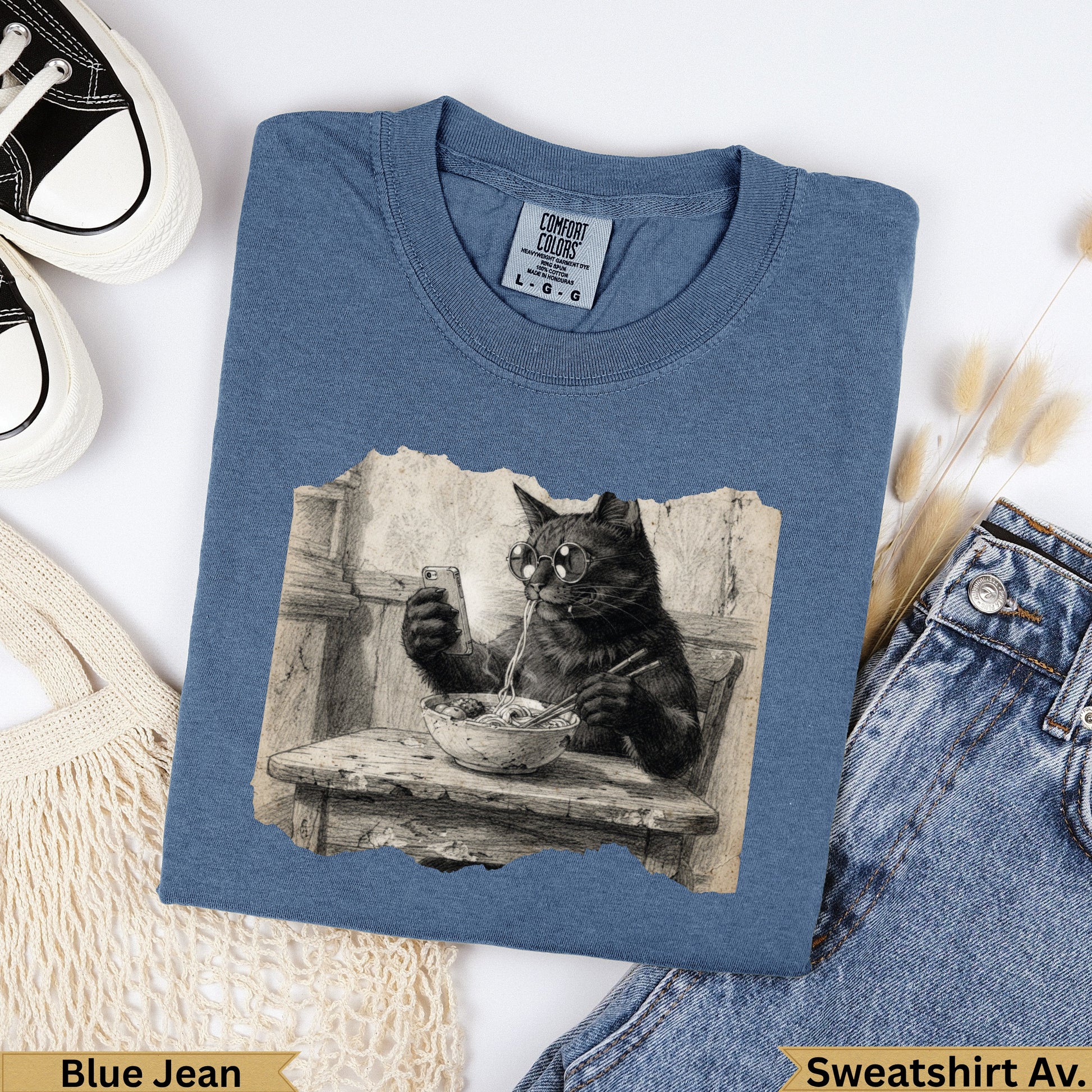 Cat wearing glasses eating ramen from a bowl, on a blue t-shirt.