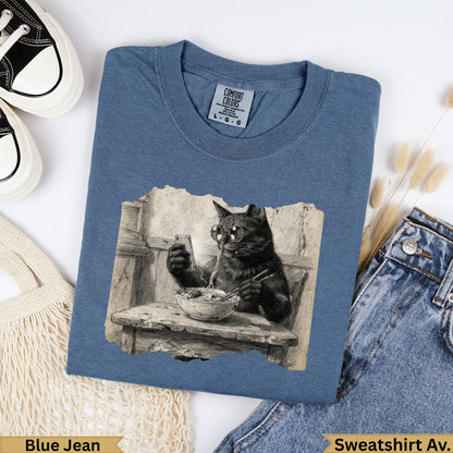Cat wearing glasses eating ramen from a bowl, on a blue t-shirt.