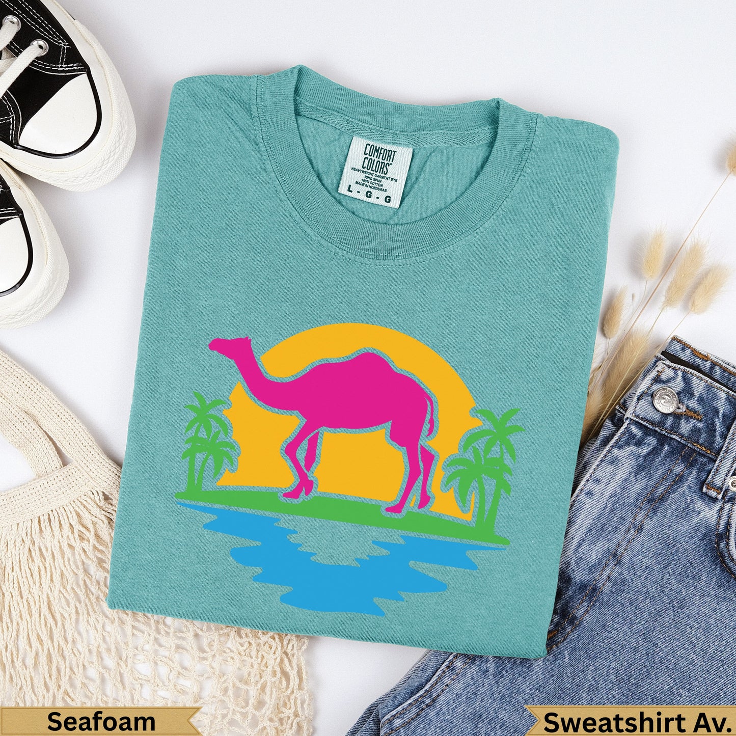 Teal t-shirt with pink camel, yellow sun, palm trees, and blue water graphic.