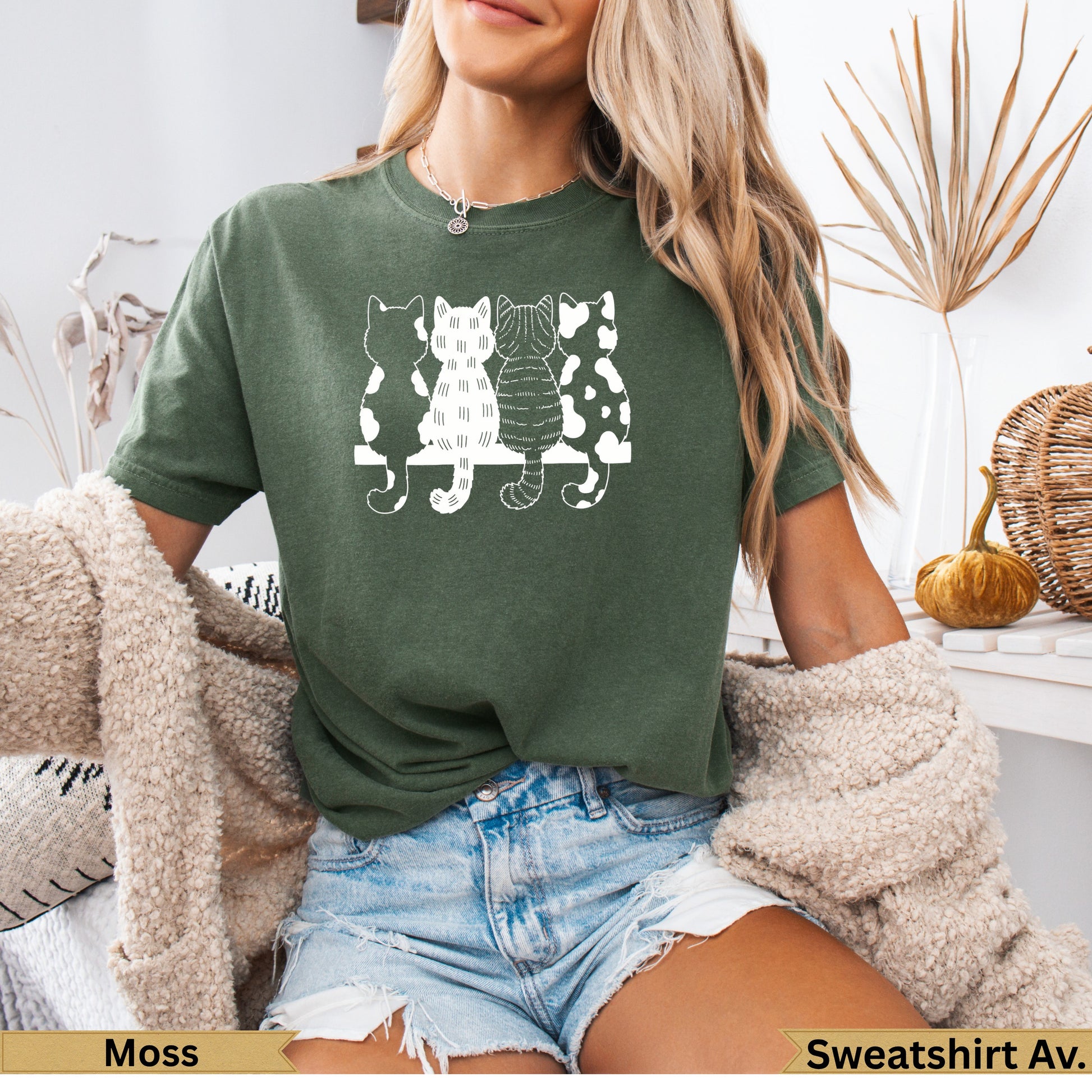 Woman wearing olive green t-shirt with three black and white cartoon cats.