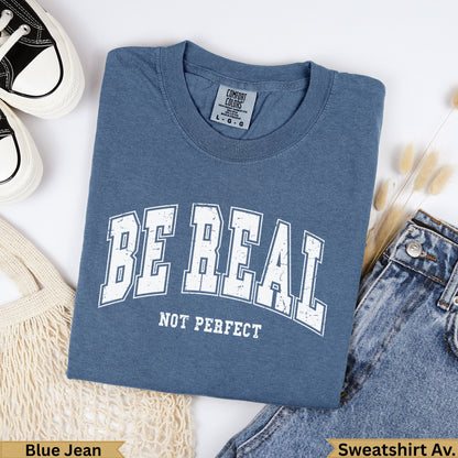 Blue t-shirt with "BE REAL NOT PERFECT" text, garment dyed.