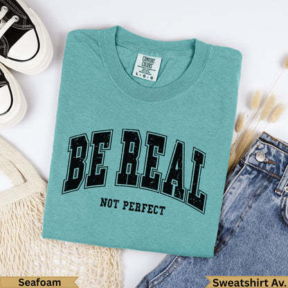 Teal Comfort Colors "BE REAL NOT PERFECT" graphic t-shirt with jeans.