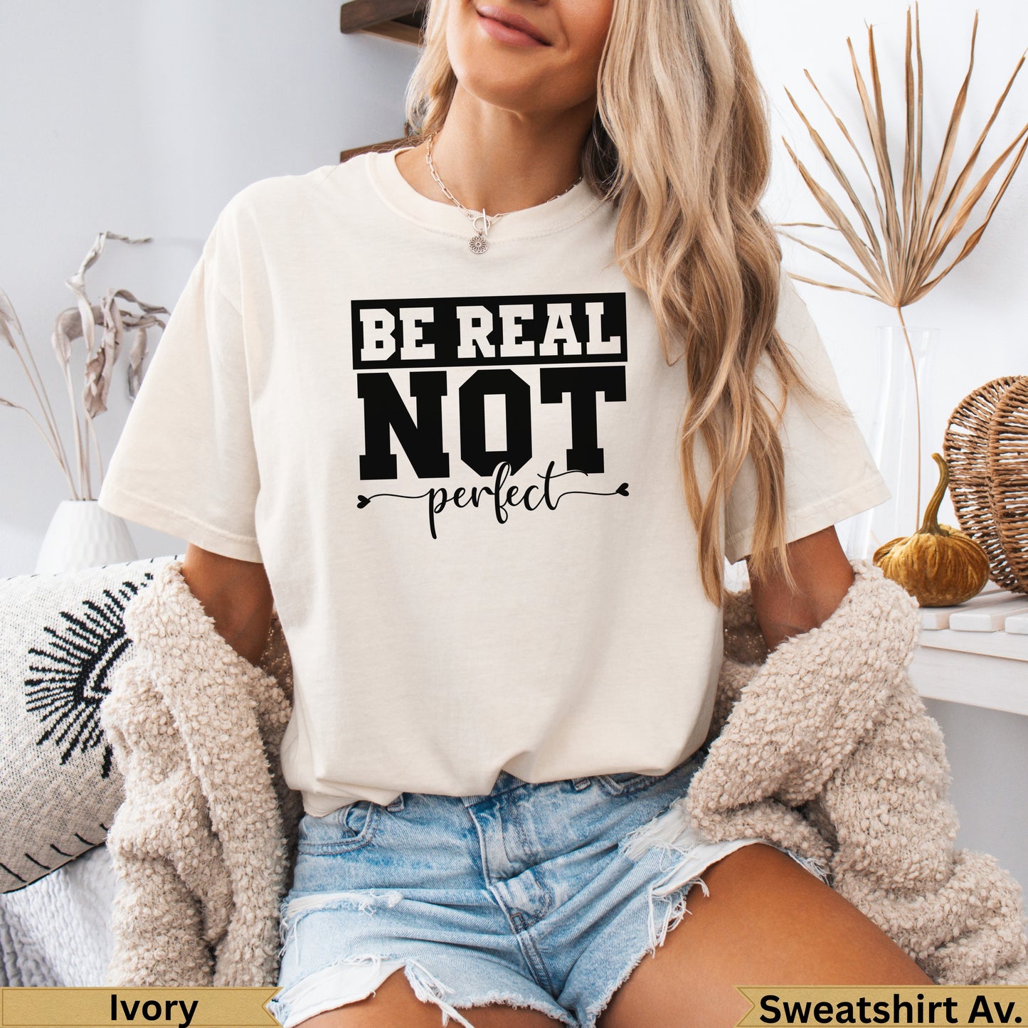 Cream sweatshirt with "BE REAL NOT perfect" graphic, worn by a woman.