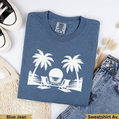 Blue denim t-shirt with white palm trees, sun, and chairs graphic.