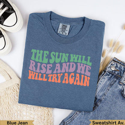 Blue crewneck sweatshirt with "The Sun Will Rise And We Will Try Again" text.