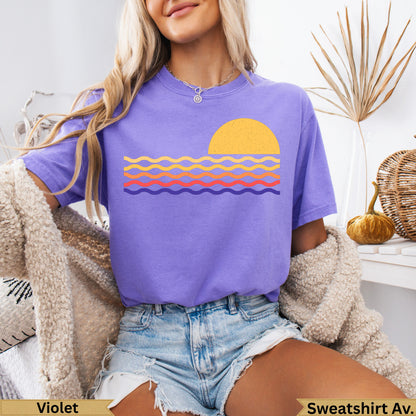 Purple t-shirt with stylized orange sun and colorful wavy lines.