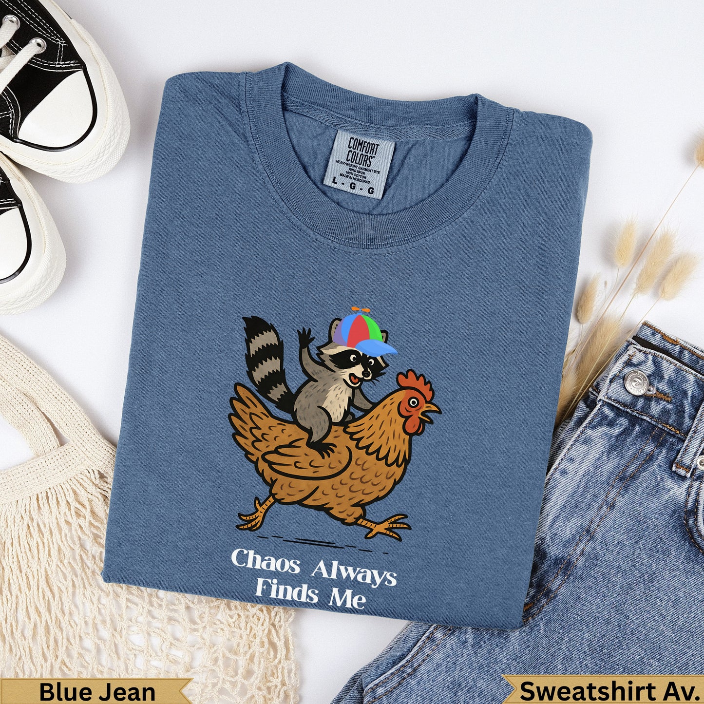 Raccoon riding chicken with "Chaos Always Finds Me" text on blue shirt.