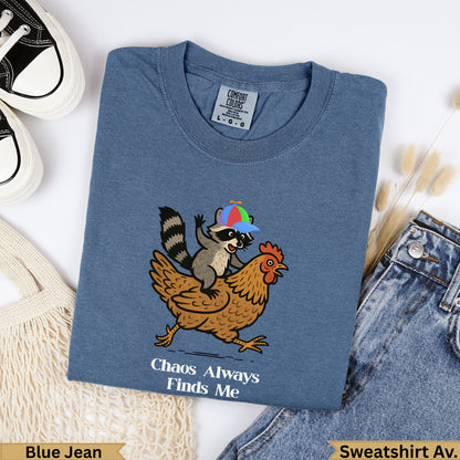 Raccoon riding chicken with "Chaos Always Finds Me" text on blue shirt.