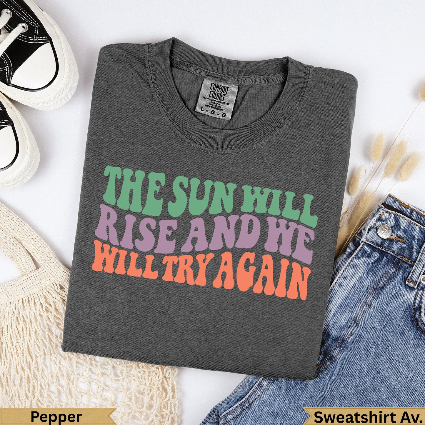 Dark grey t-shirt with "The Sun Will Rise And We Will Try Again" in colorful text.