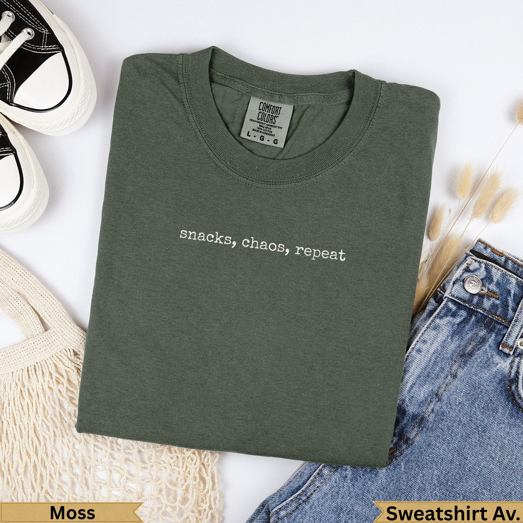 Olive green t-shirt with "snacks, chaos, repeat" text.