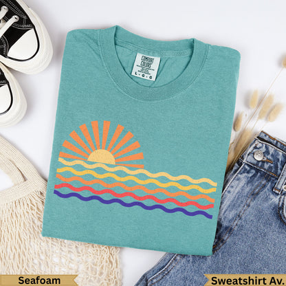 Teal Comfort Colors t-shirt with colorful wavy sun graphic, labeled "Seafoam" and "Sweatshirt Av.".