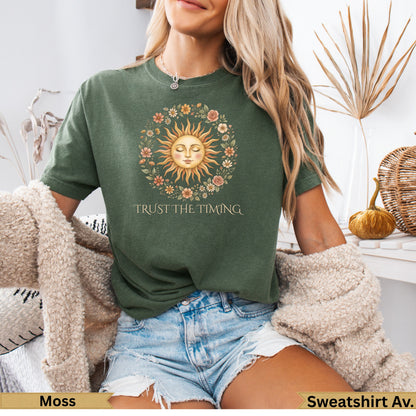 Moss green t-shirt with sun and floral graphic and "Trust The Timing" text.