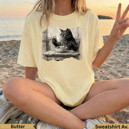Black cat eating from a bowl on a graphic t-shirt.