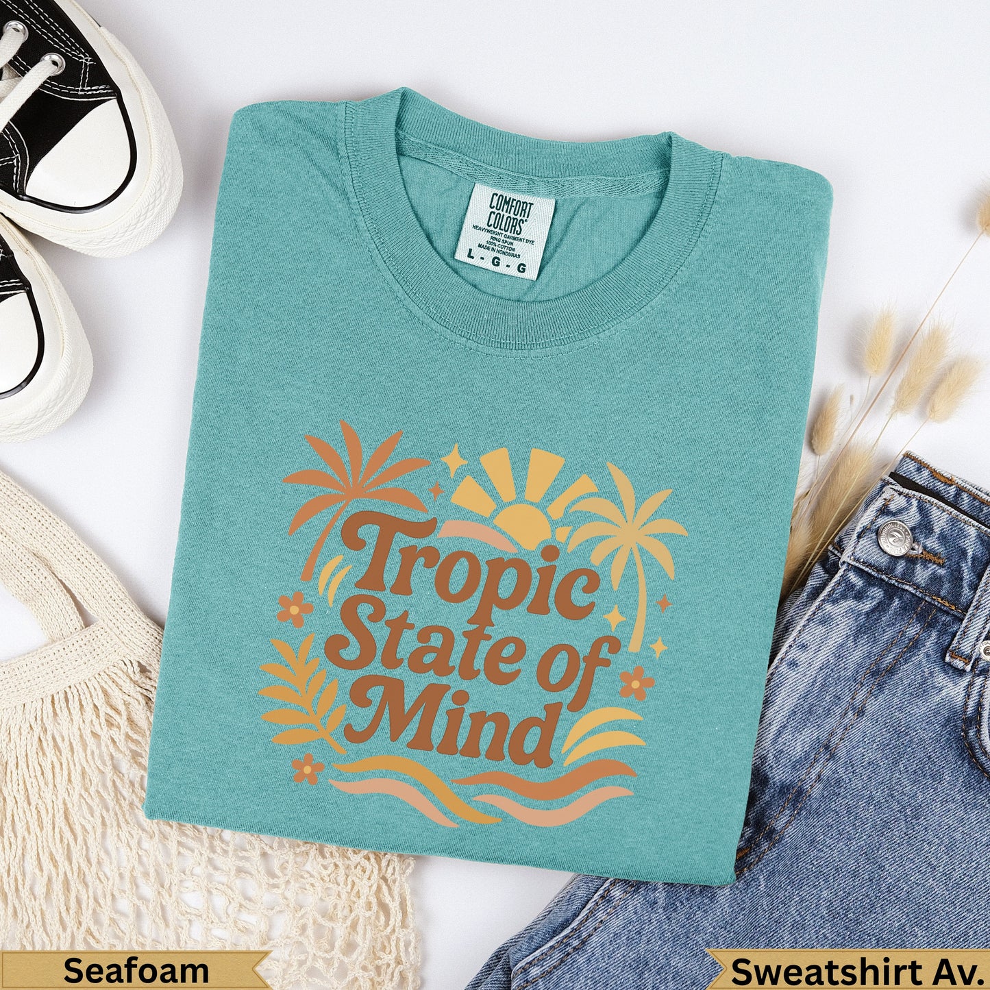 Teal "Tropic State of Mind" graphic sweatshirt on a flat lay with jeans.