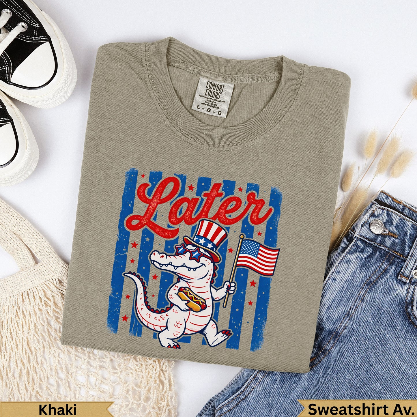 Khaki crewneck sweatshirt with alligator wearing sunglasses and holding hot dog with American flag.