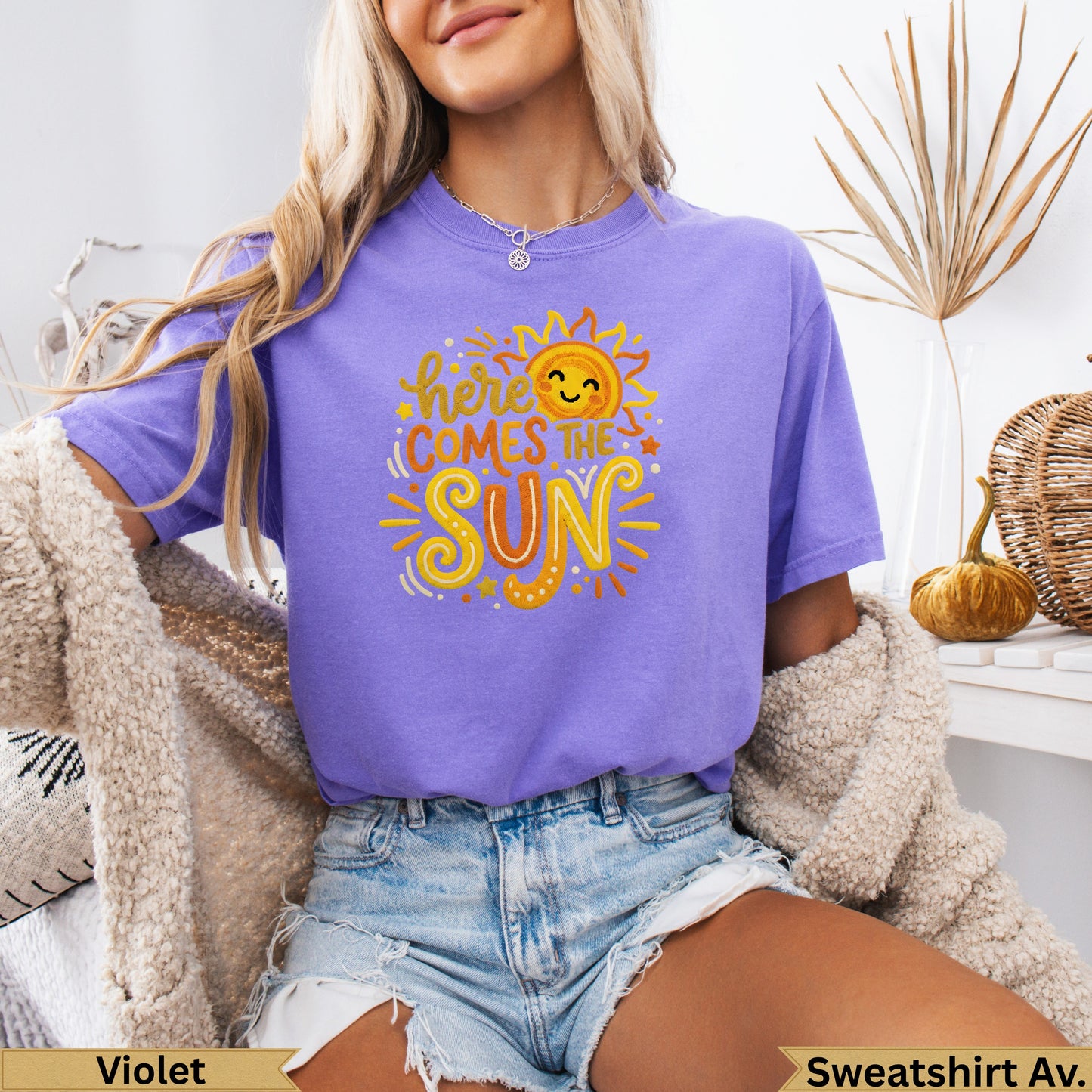 Purple t-shirt with smiling sun and text "here comes the sun".