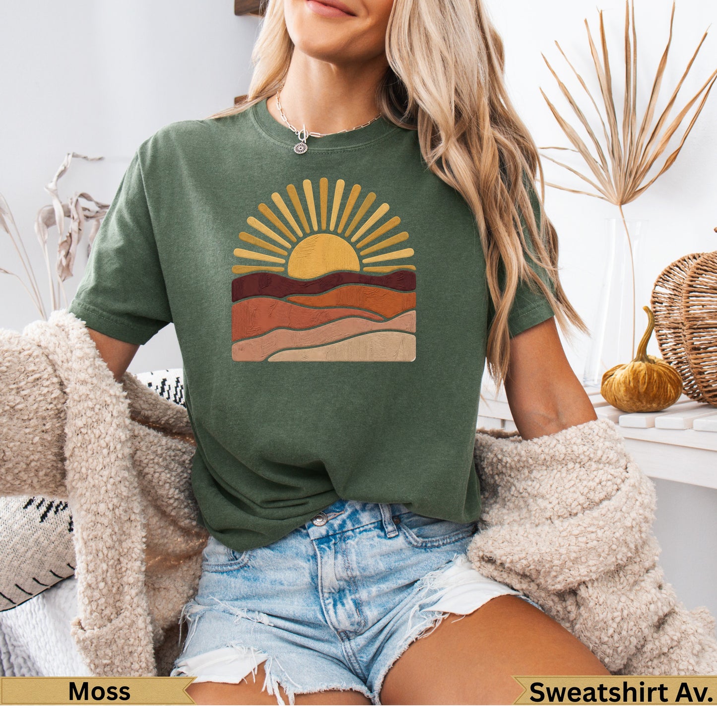 Green t-shirt with stylized sun and layered landscape graphic.