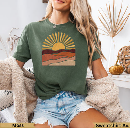 Green t-shirt with stylized sun and layered landscape graphic.