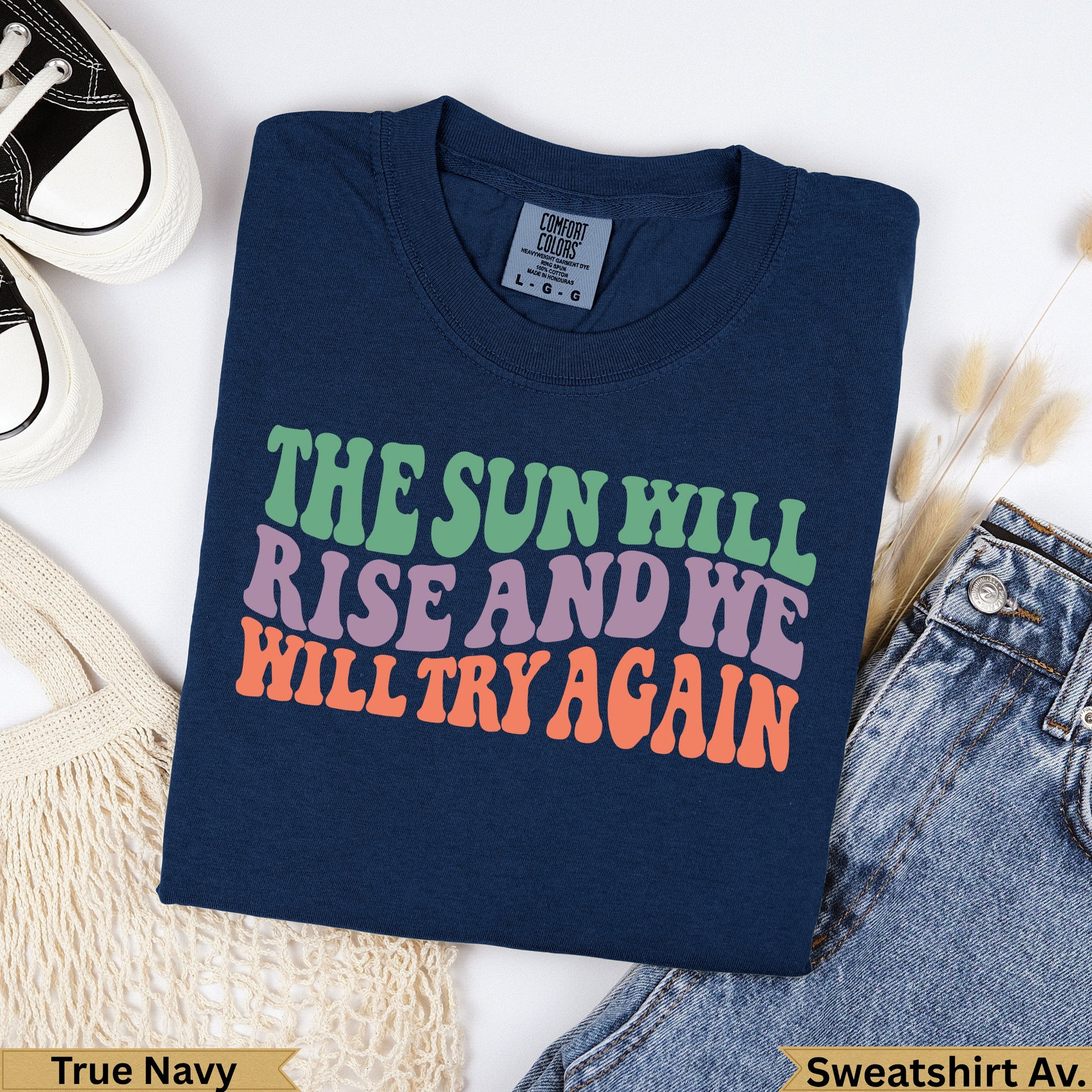 Navy sweatshirt with "The Sun Will Rise And We Will Try Again" text.