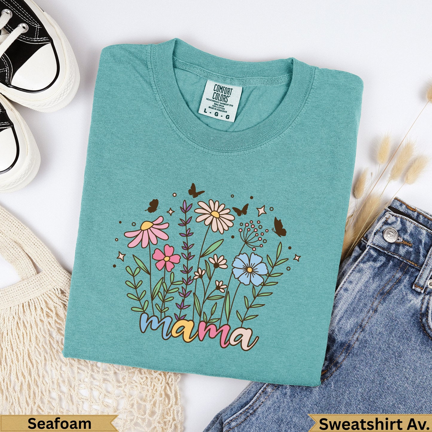 Teal t-shirt with "mama" text and floral design, placed on a white background.
