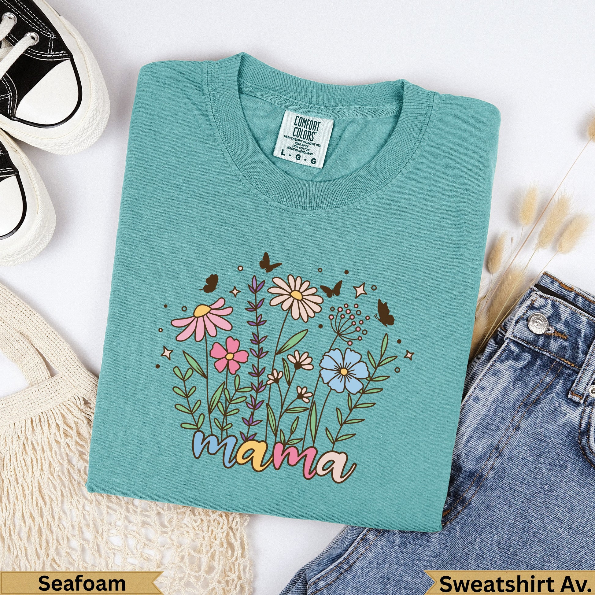 Teal t-shirt with "mama" text and floral design, placed on a white background.