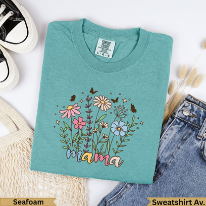 Teal t-shirt with "mama" text and floral design, placed on a white background.