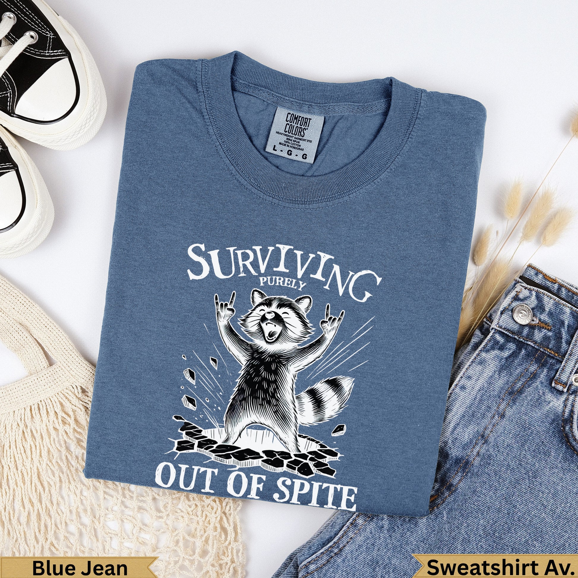 Blue graphic t-shirt with a raccoon saying "Surviving Out of Spite".