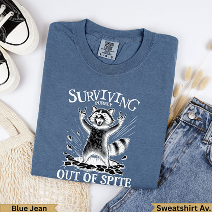 Blue graphic t-shirt with a raccoon saying "Surviving Out of Spite".