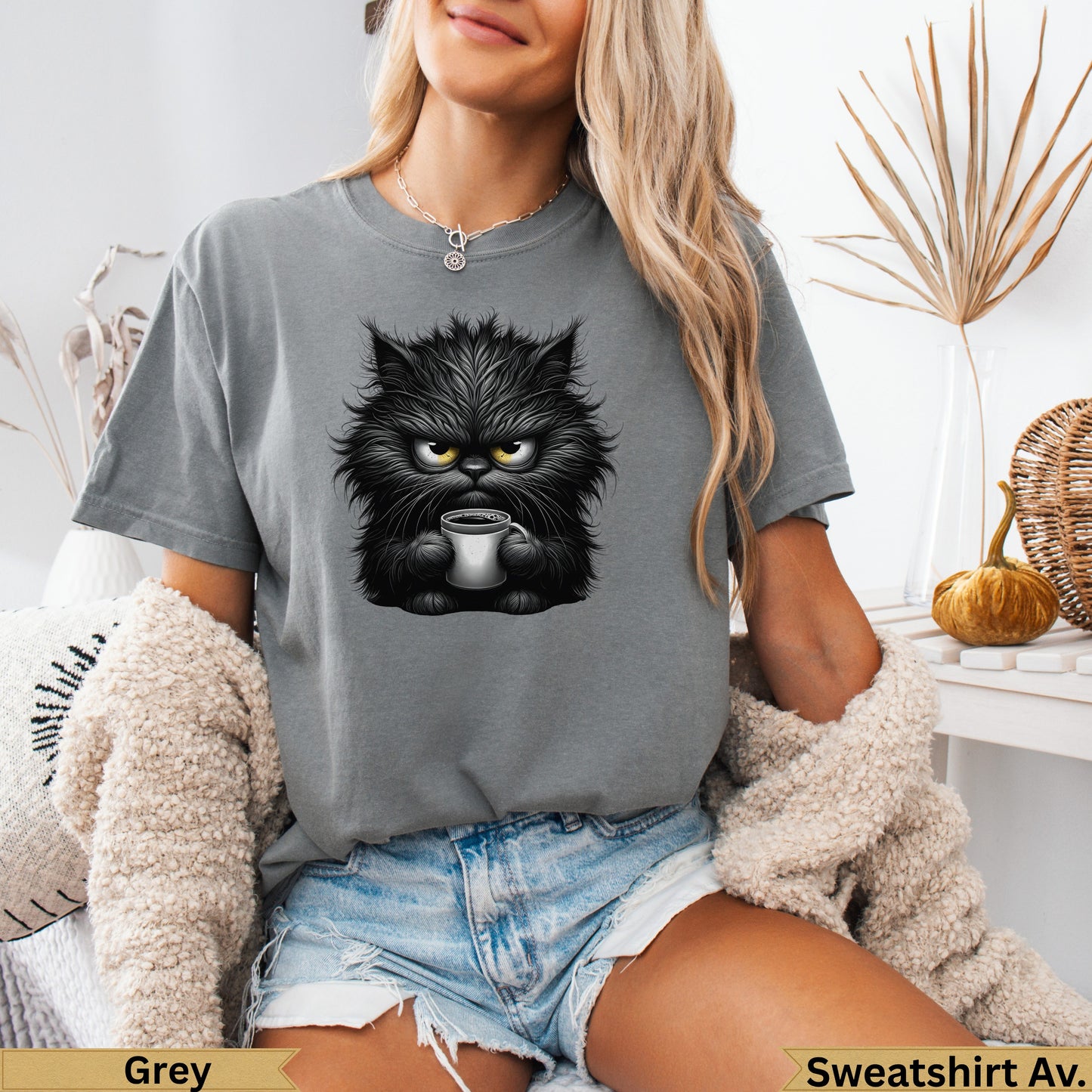 Furry black cat with yellow eyes holding a coffee mug, wearing a grey t-shirt.