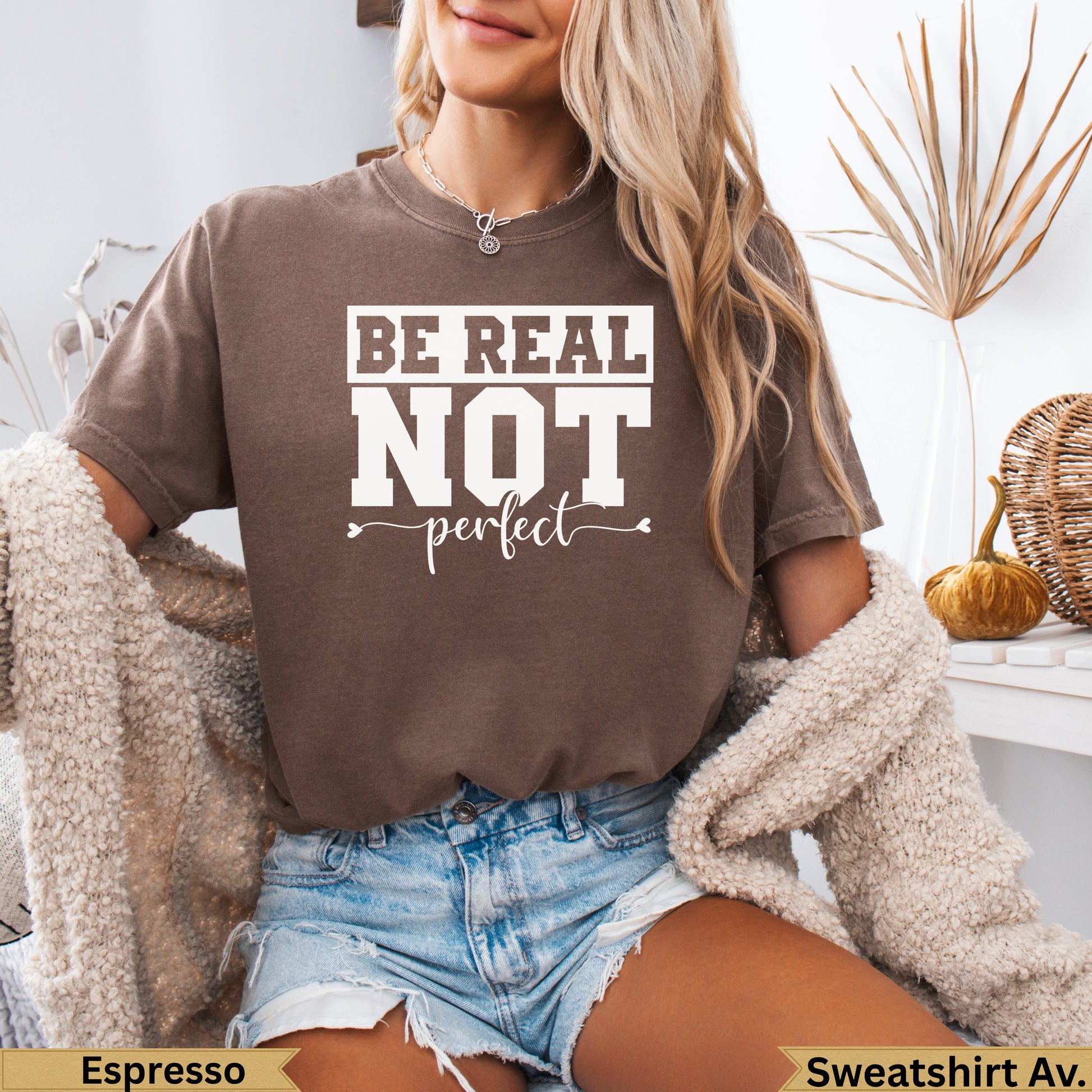Brown t-shirt with "Be Real Not" text, worn by a person.