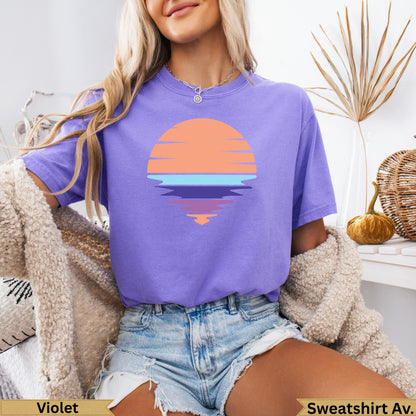 Purple t-shirt with orange sunset graphic and reflection on water.