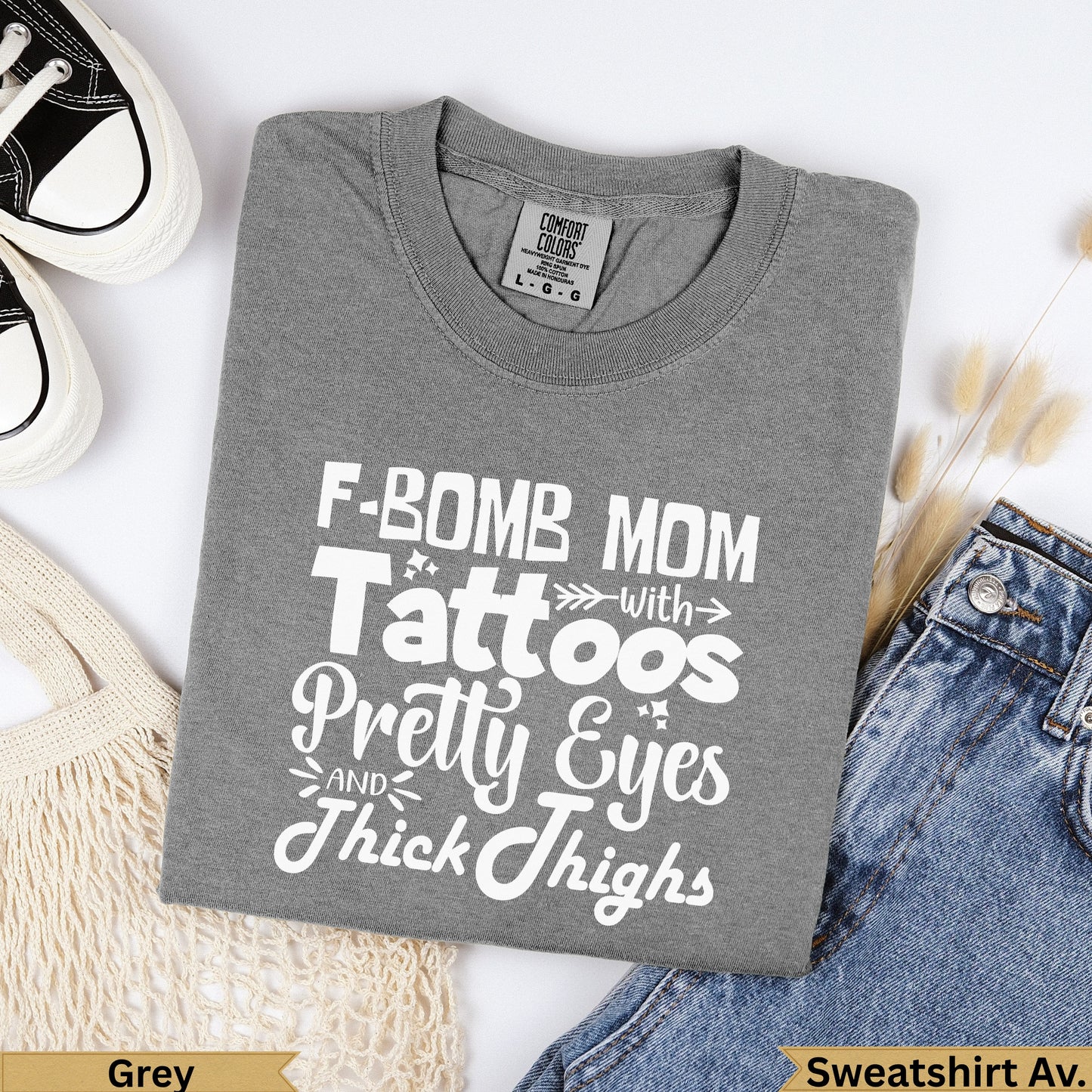 Grey t-shirt with "F-Bomb Mom" text, placed on jeans.