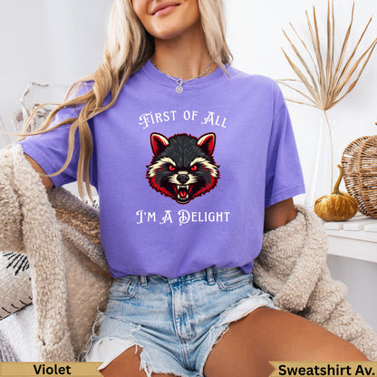 Purple t-shirt with red-eyed raccoon graphic and text "First of all I'm a delight".