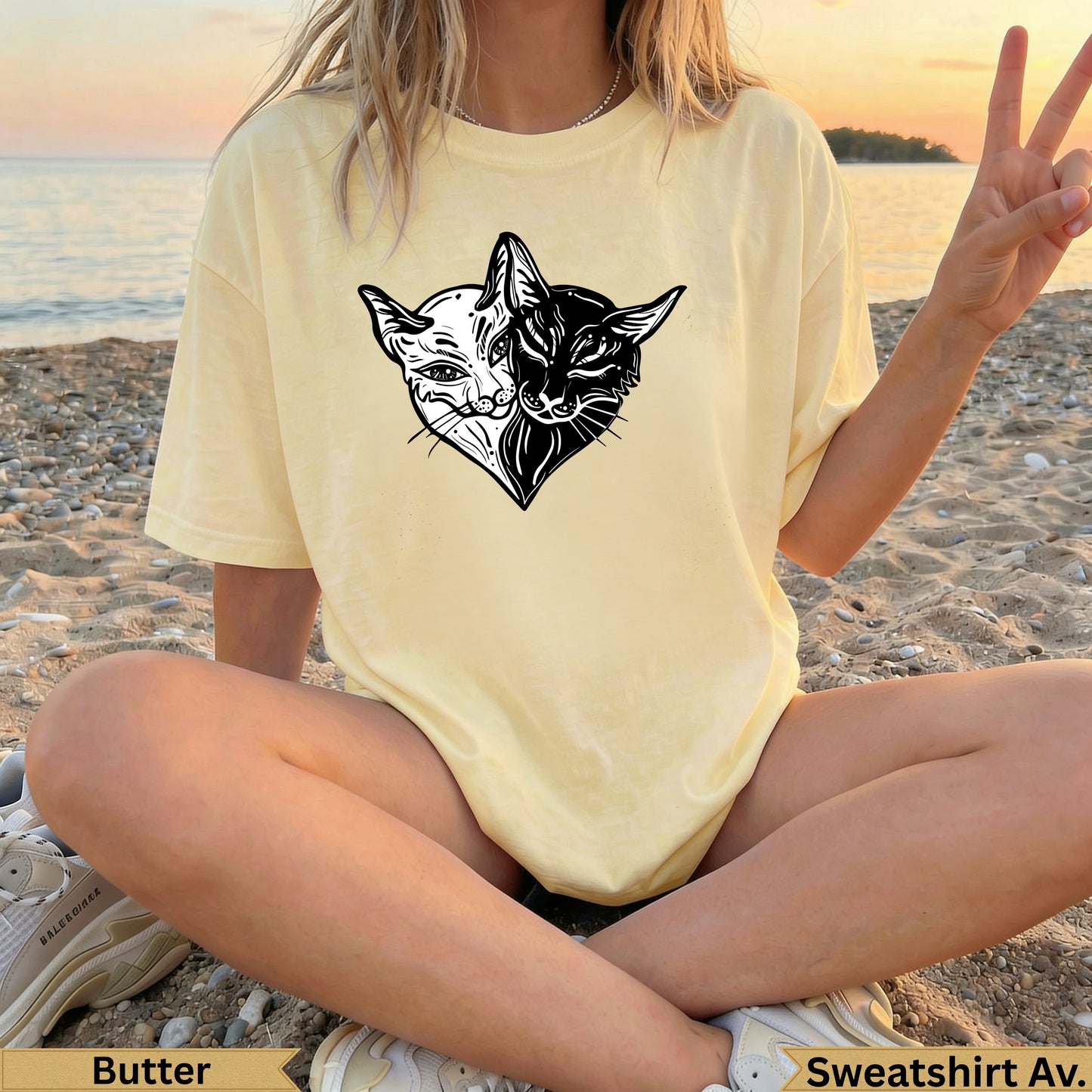 Cream t-shirt with yin-yang cat heart graphic, person sitting on beach.