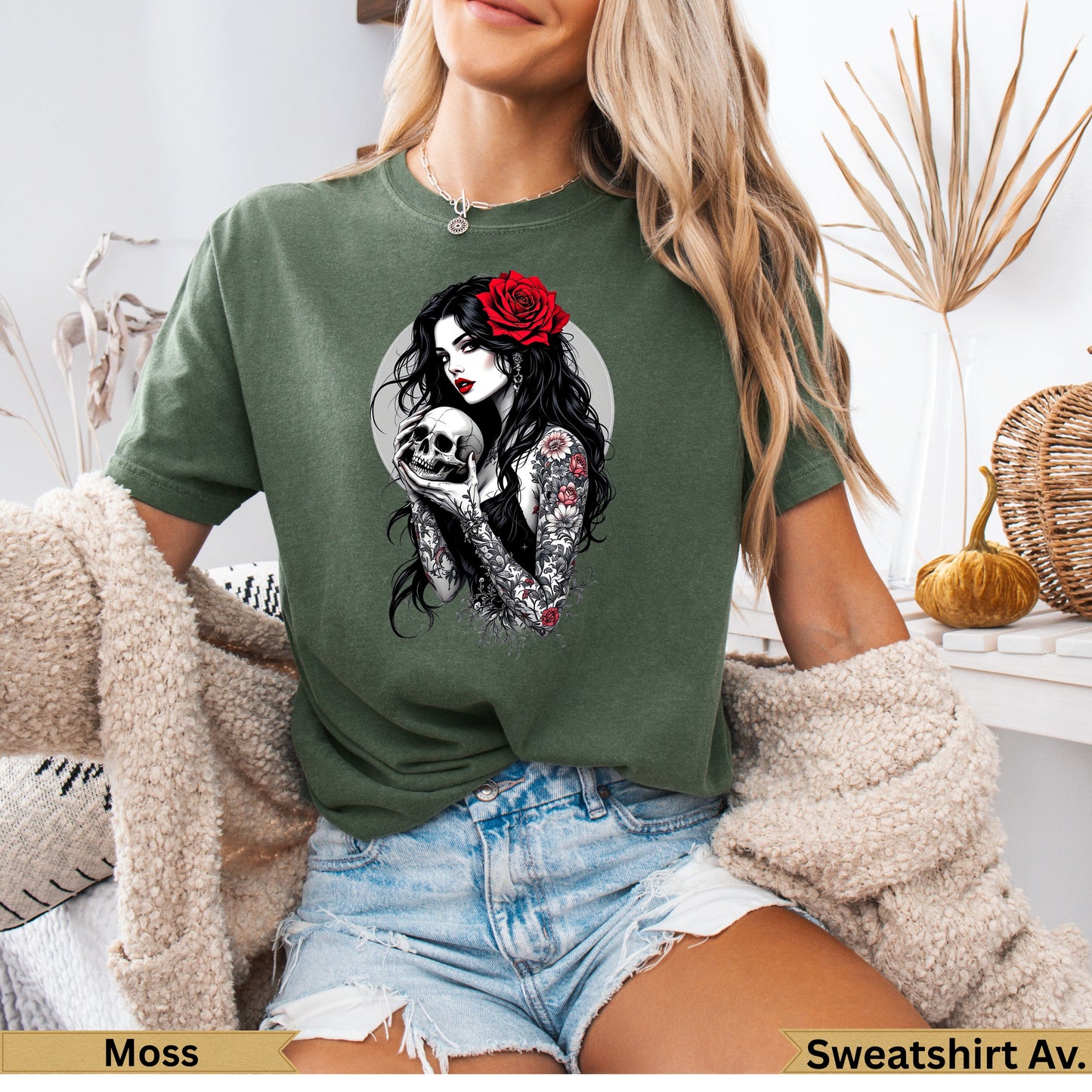 Woman in moss green t-shirt holding a skull with red rose in hair.