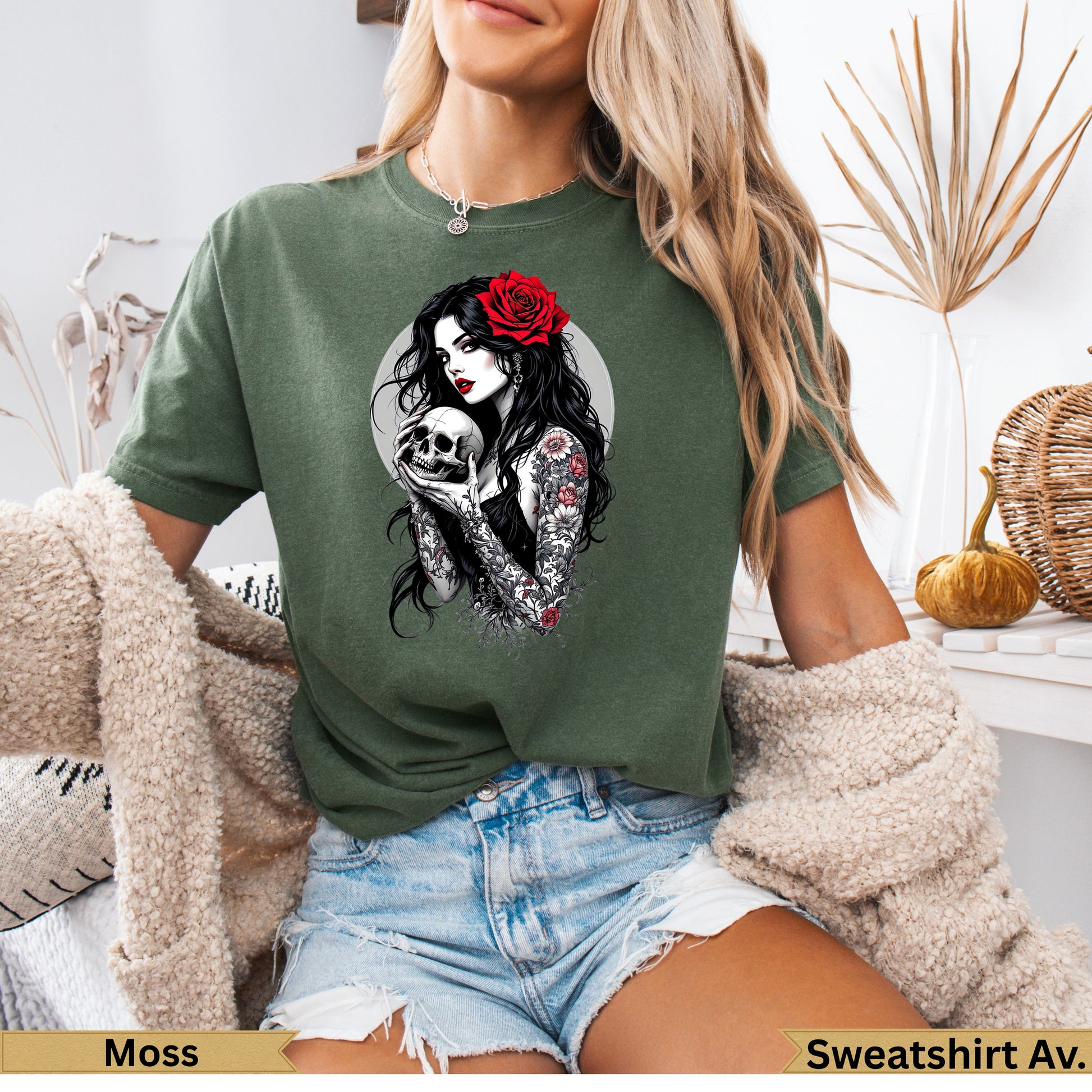 Woman in moss green t-shirt holding a skull with red rose in hair.