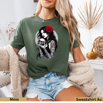 Woman in moss green t-shirt holding a skull with red rose in hair.