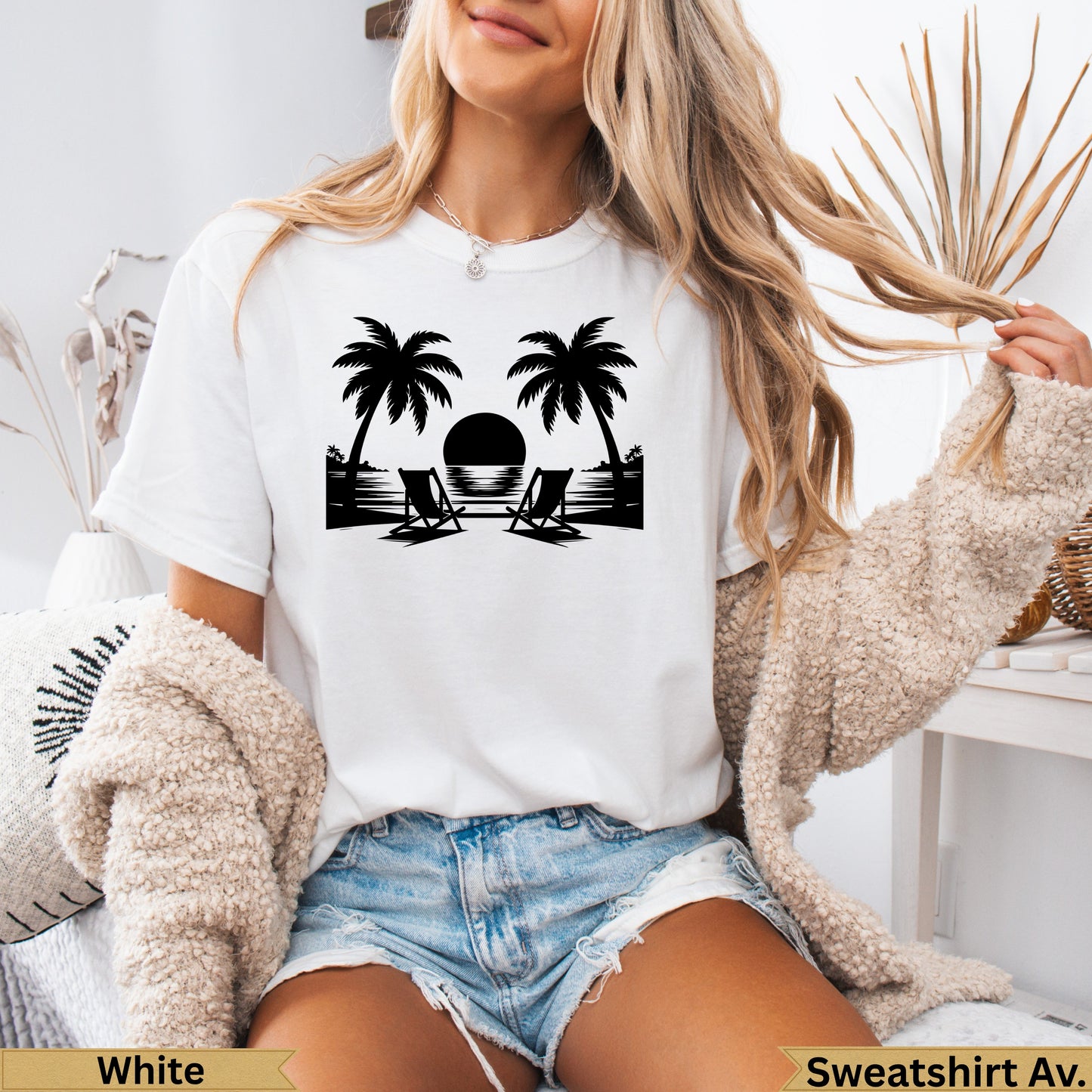 White t-shirt with black silhouette of palm trees, beach chairs, and sunset.